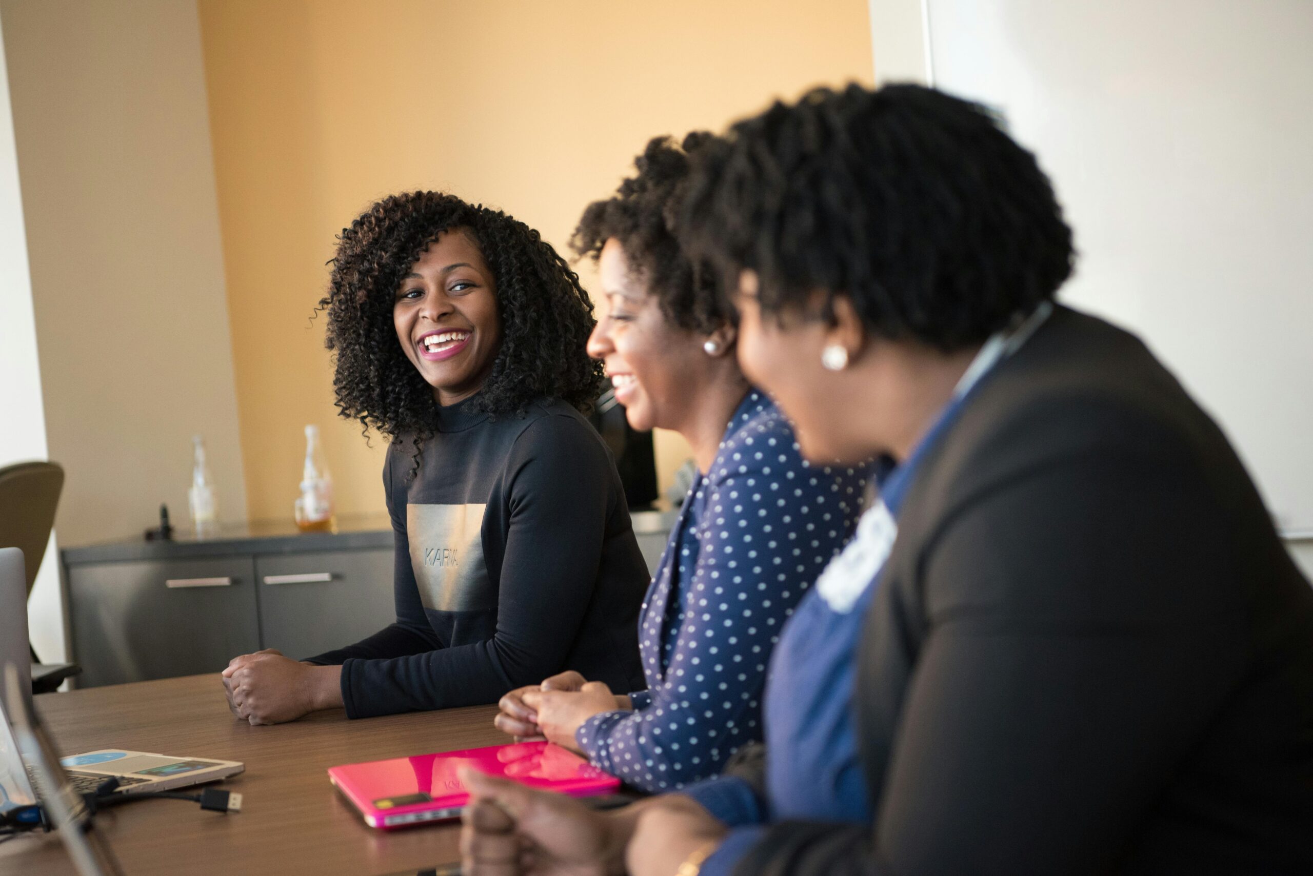 Three black women in a happy office meeting, engaging in teamwork.