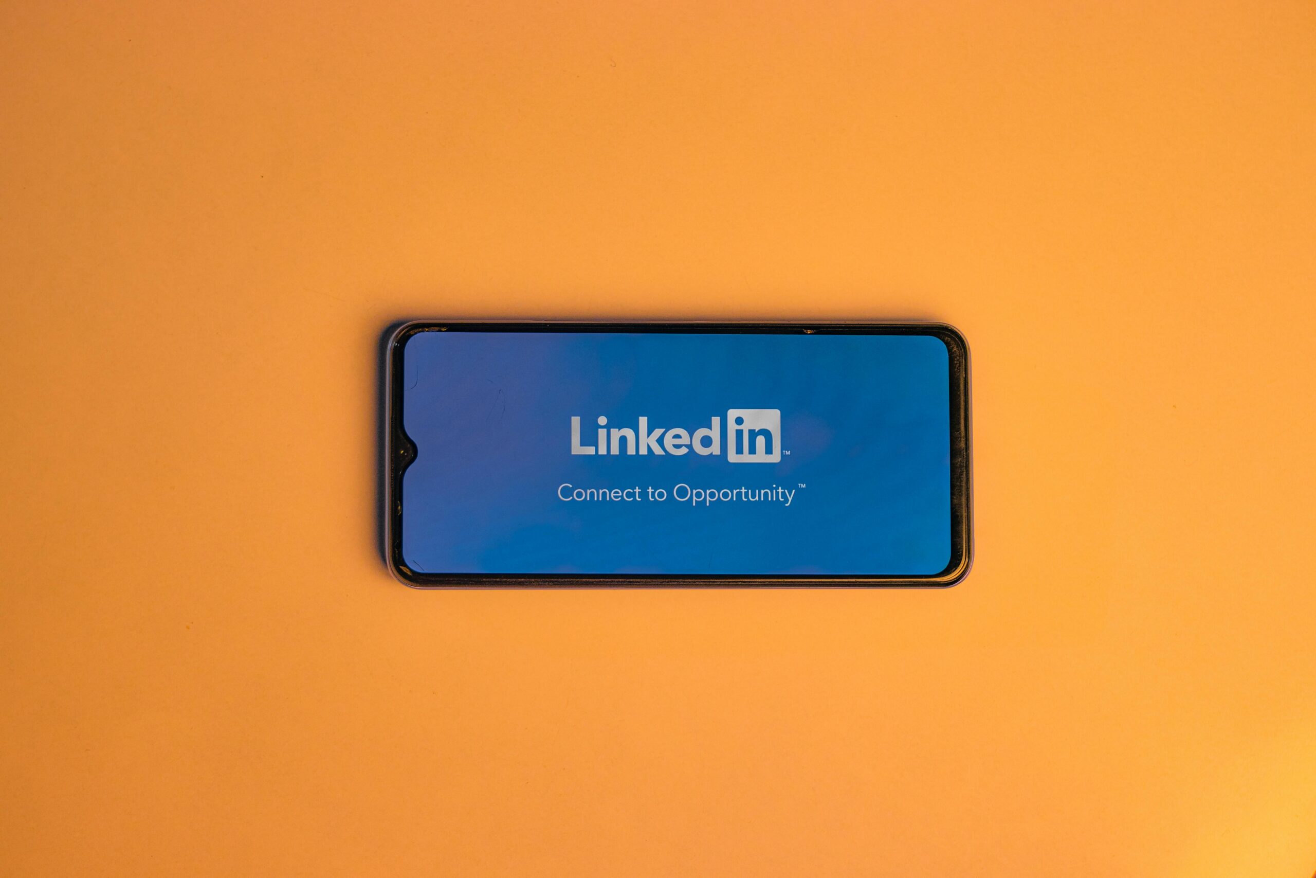 Smartphone showing LinkedIn login on vibrant orange background, symbolizing connectivity.