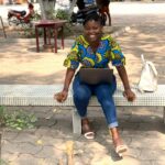 Smiling African woman on a bench using a laptop outdoors in Benin, embracing technology with joy.